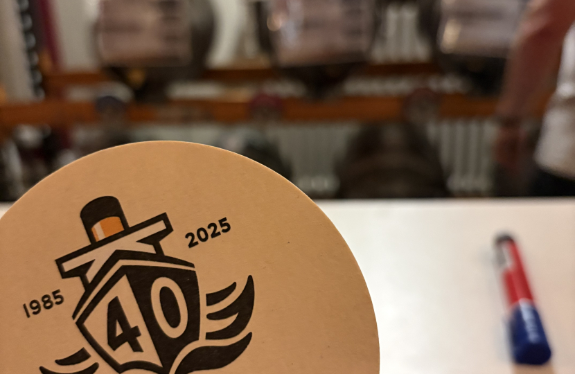 A Titanic Brewery beer mat held up in front of some beer casks.